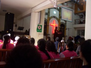 Pastor Liao speaking from the pulpit while the choir looks on.