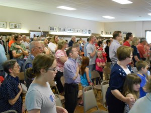 The audience faces the US flag and says the Pledge of Allegiance, right hand over your heart.